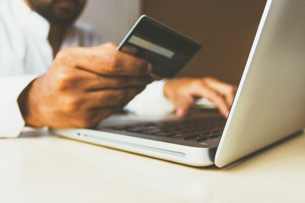 Hands using a credit card beside a laptop during an online transaction.