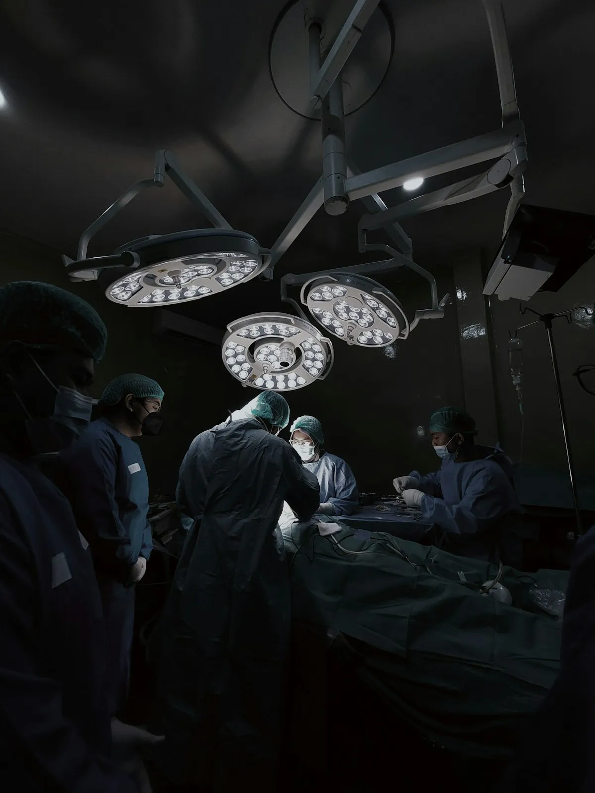 Medical team in surgical scrubs gathered around a hospital operating table beneath surgical lights