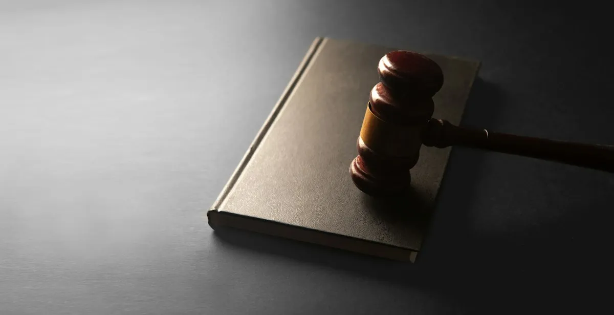 Wooden judge's gavel resting on a closed law book in dramatic side light